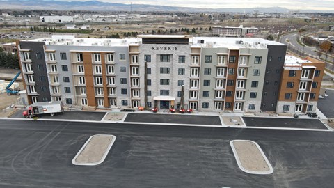 A large multi-story apartment building named Reverie sits empty in a parking lot.