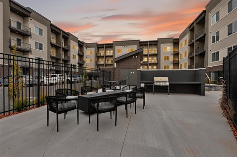 A patio with chairs and a table is surrounded by apartment buildings.