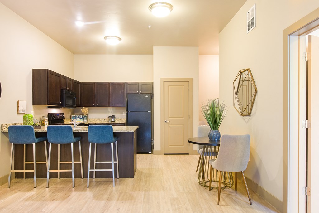 a kitchen with a bar and stools next to a living room with a refrigerator at Sugar House Apartments By Urbana, Salt Lake City, UT, 84105