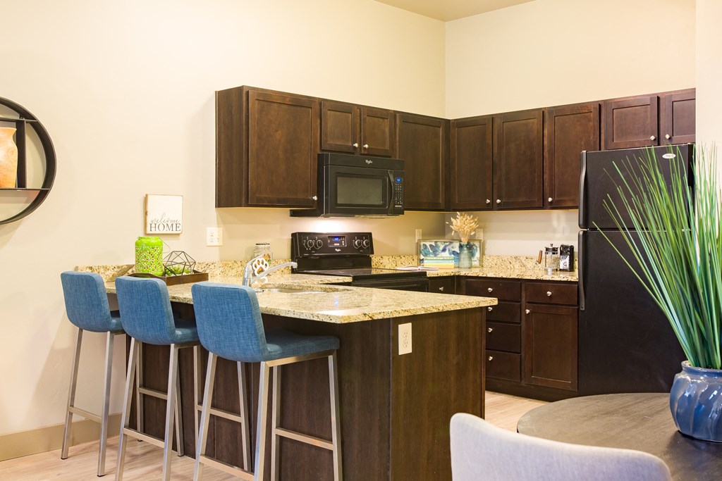 a kitchen with an island with bar stools and a black refrigerator at Sugar House Apartments By Urbana, Salt Lake City, UT, 84105