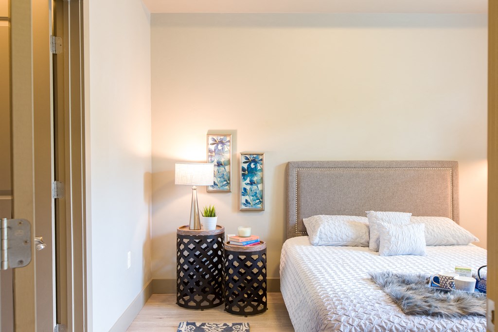 a bedroom with a bed and a nightstand with plants and a lamp at Sugar House Apartments By Urbana, Salt Lake City, UT, 84105