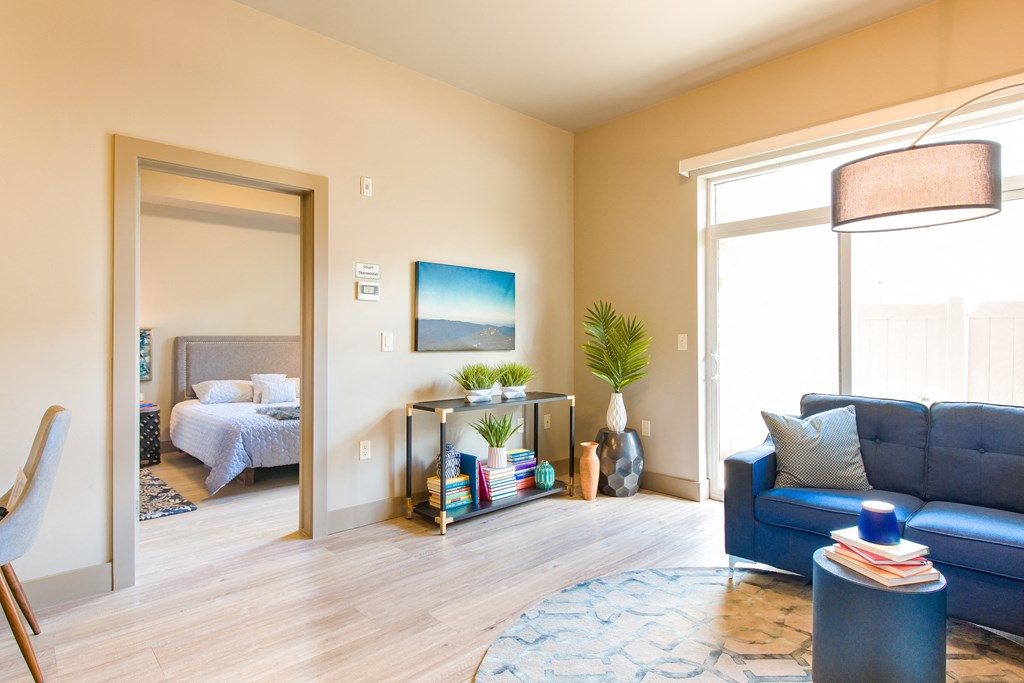 a living room with a blue couch and a lamp and a bedroom in the background at Sugar House Apartments By Urbana, Salt Lake City, UT, 84105