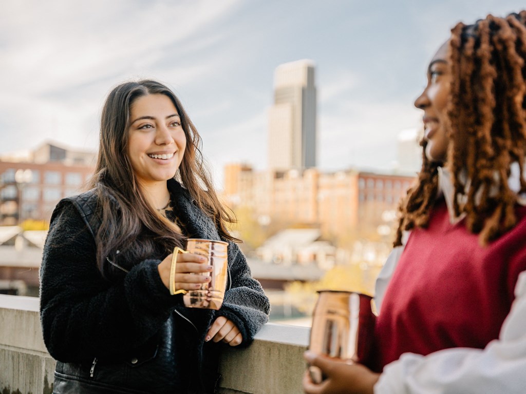 two women standing on a balcony drinking coffee and talking