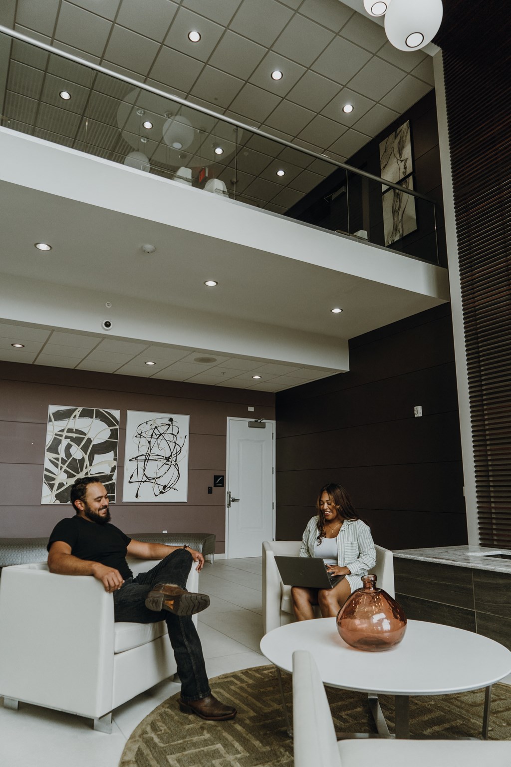 a man and a woman sitting in a lobby with their laptops
