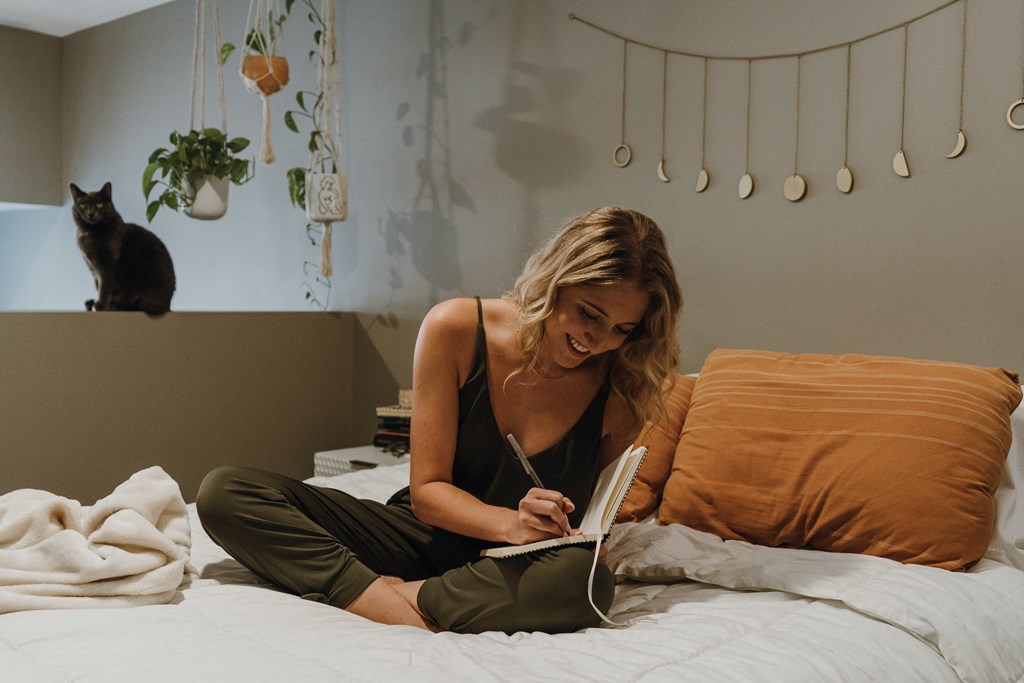 a woman sitting on a bed reading a book with a cat in the background