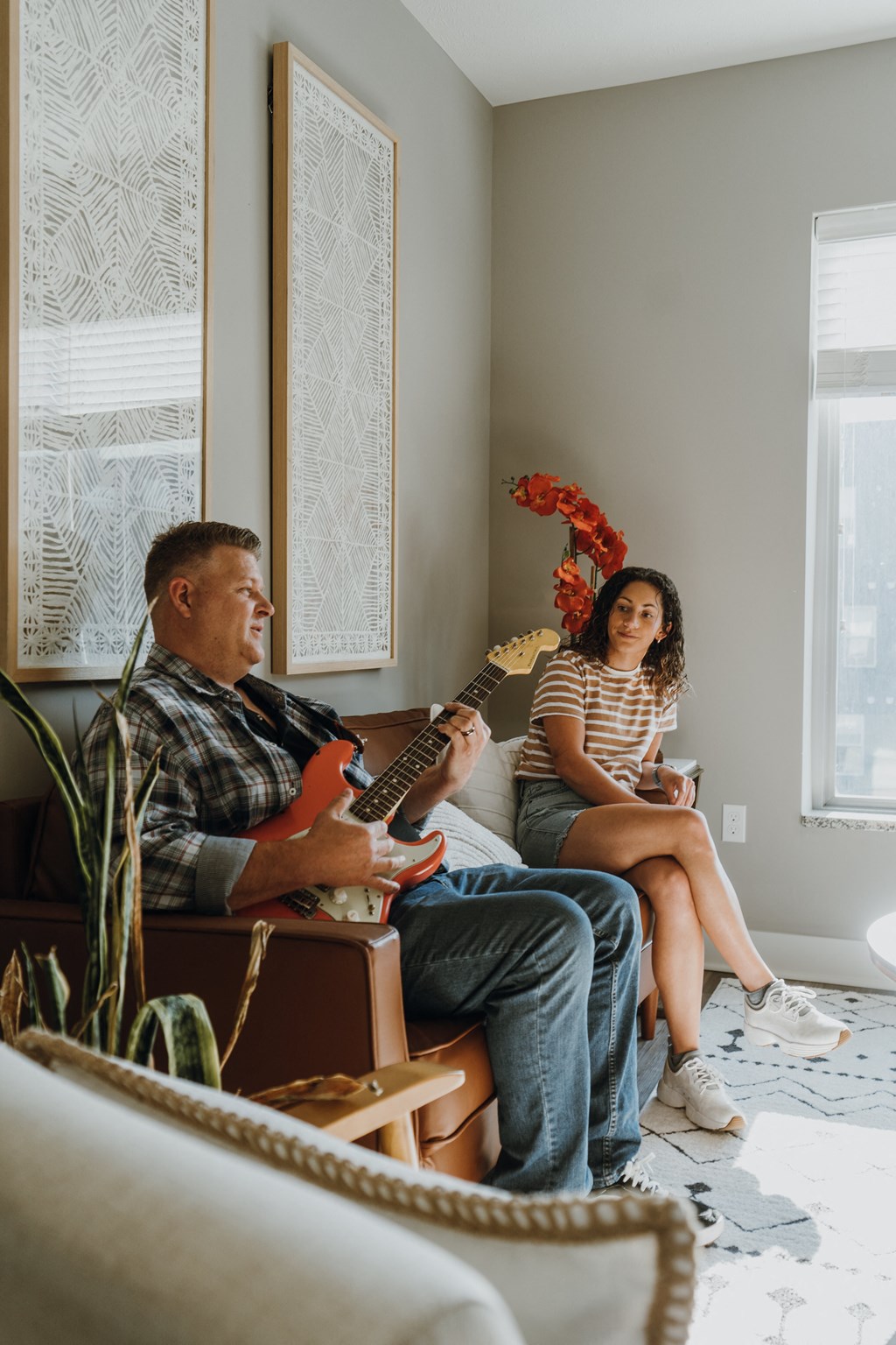 a man playing guitar and a woman sitting on a chair in a living room