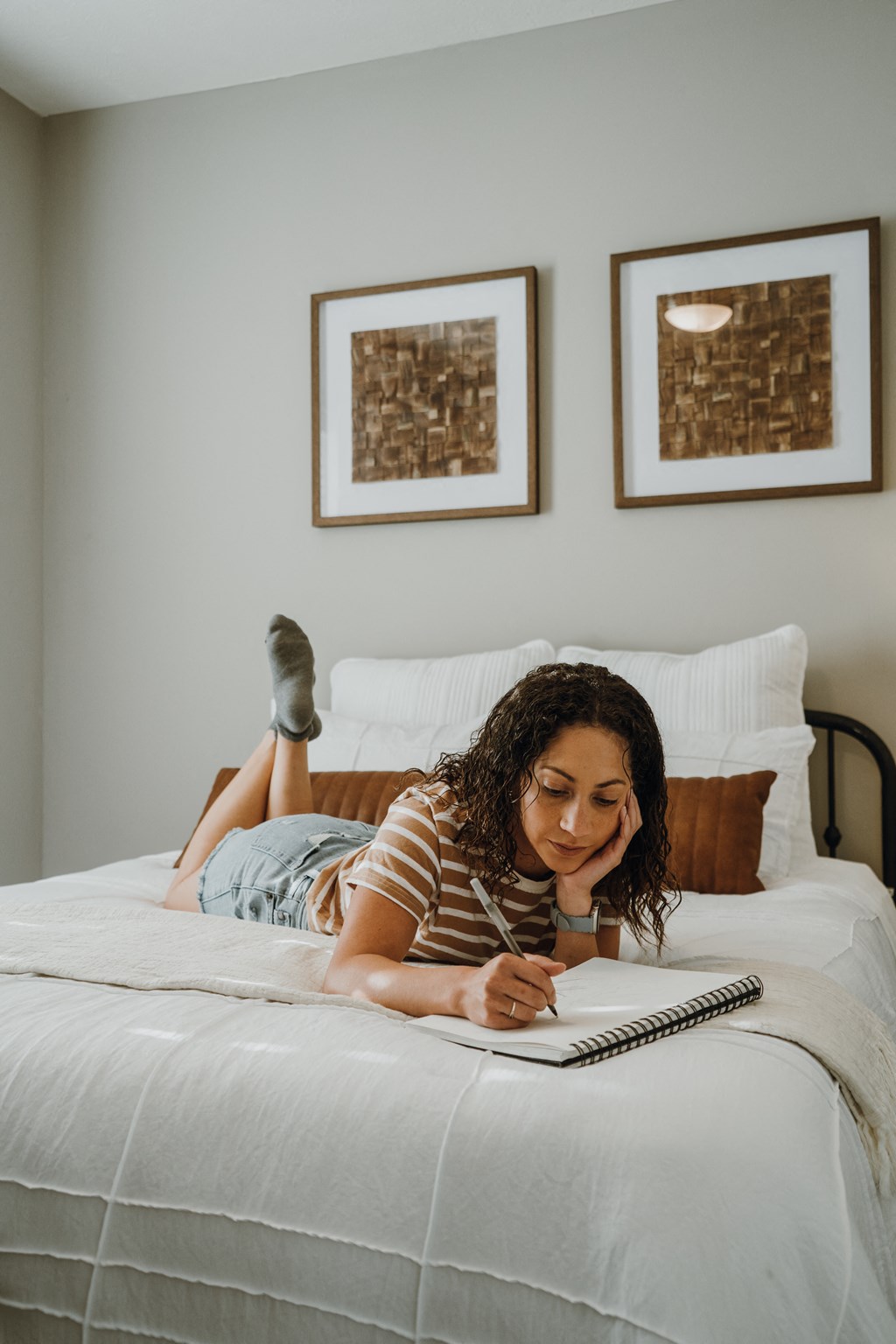 a woman laying on a bed writing in a notebook