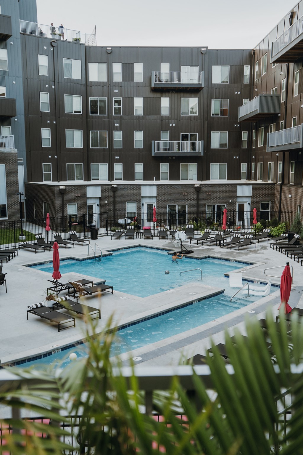 an apartment swimming pool with tables and umbrellas in front of a building