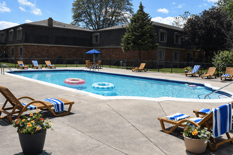 A pool surrounded by chairs and umbrellas with a building in the background.
