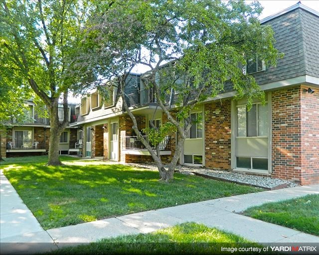 the front of an apartment building with a lawn and trees