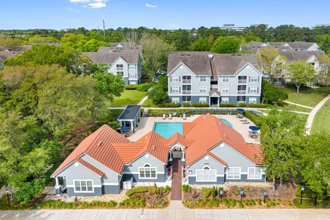 A large house with a red roof is surrounded by smaller houses and trees.