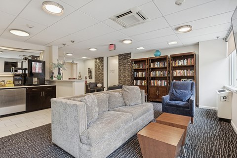 A living room with a grey couch, a blue armchair, and a bookshelf filled with books.