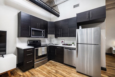 A kitchen with black cabinets and a stainless steel refrigerator.