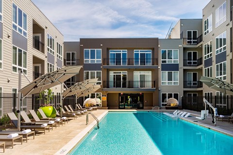 A large swimming pool in front of a building with a sun lounger.