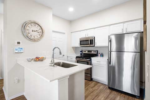 A white kitchen with a stainless steel refrigerator and a clock on the wall.