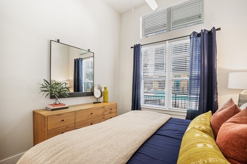 A bedroom with a bed, a dresser with a mirror and a potted plant on top.