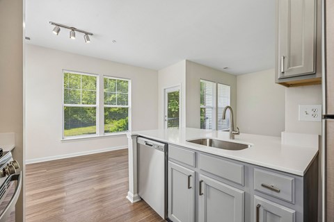 A kitchen with a white counter top and a window with blinds.
