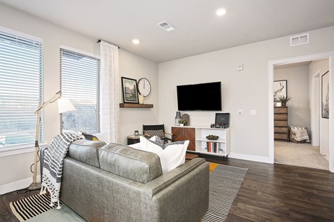 A living room with a grey couch and a flat screen TV mounted on the wall.