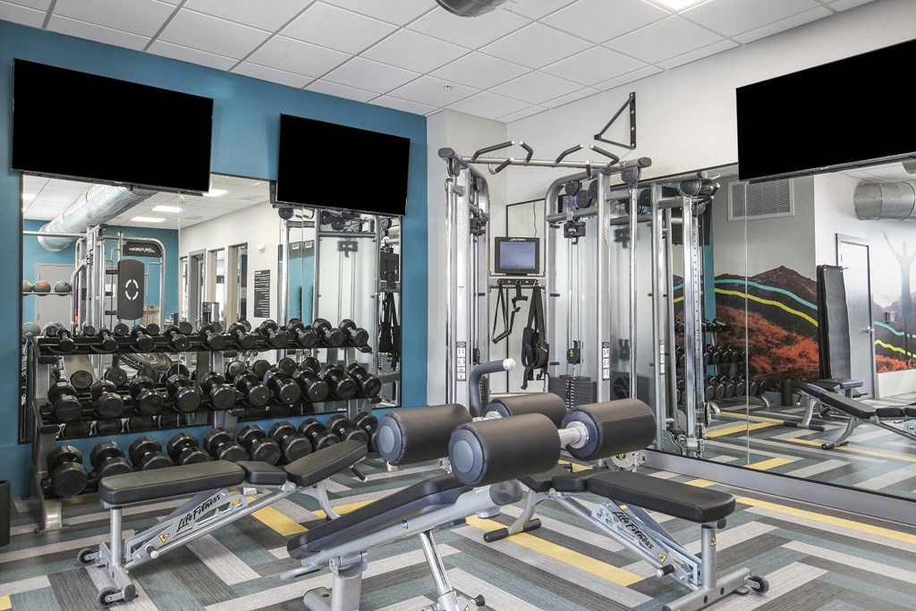 a gym with weights and cardio equipment on the floor and televisions