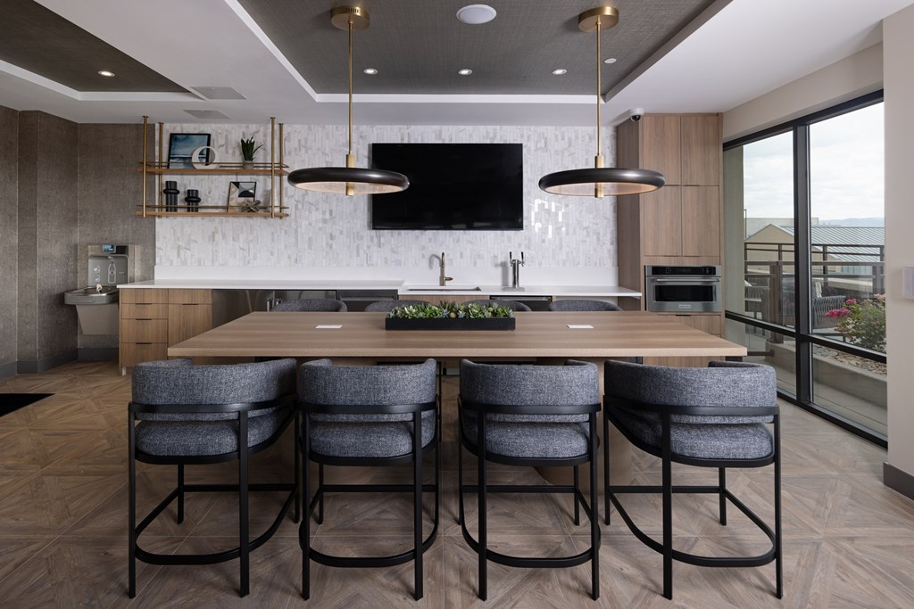 A modern kitchen with a long wooden table and grey chairs.