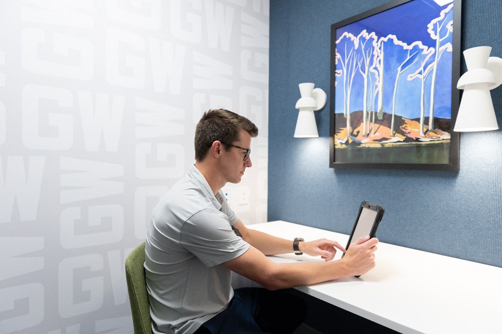 a man sitting at a desk working on a laptop computer in front of a screen