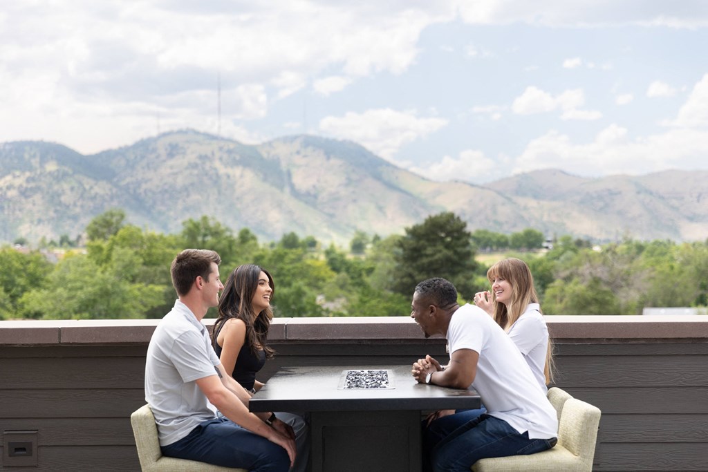 a group of people sitting at a table on a balcony with mountains in the background