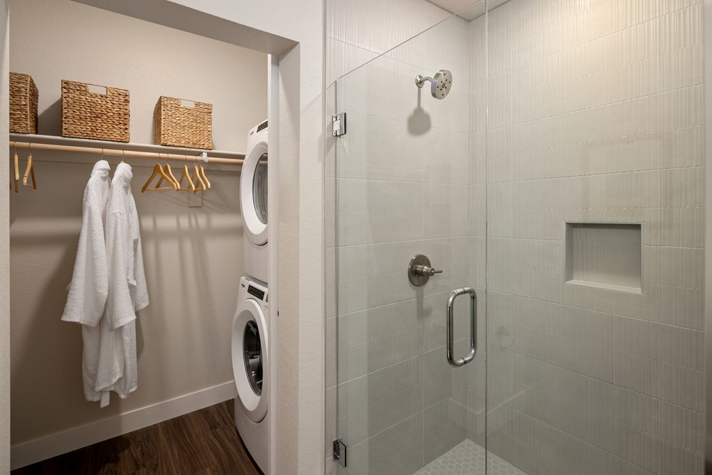 A bathroom with a white tiled shower and a white washing machine.