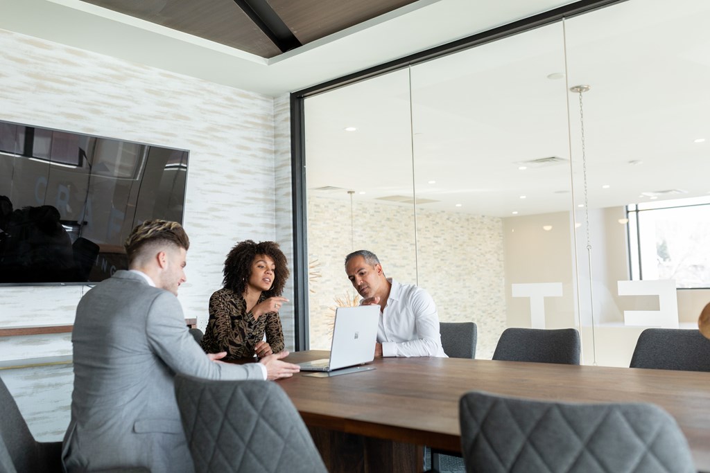 Three people are sitting around a table in a meeting room.