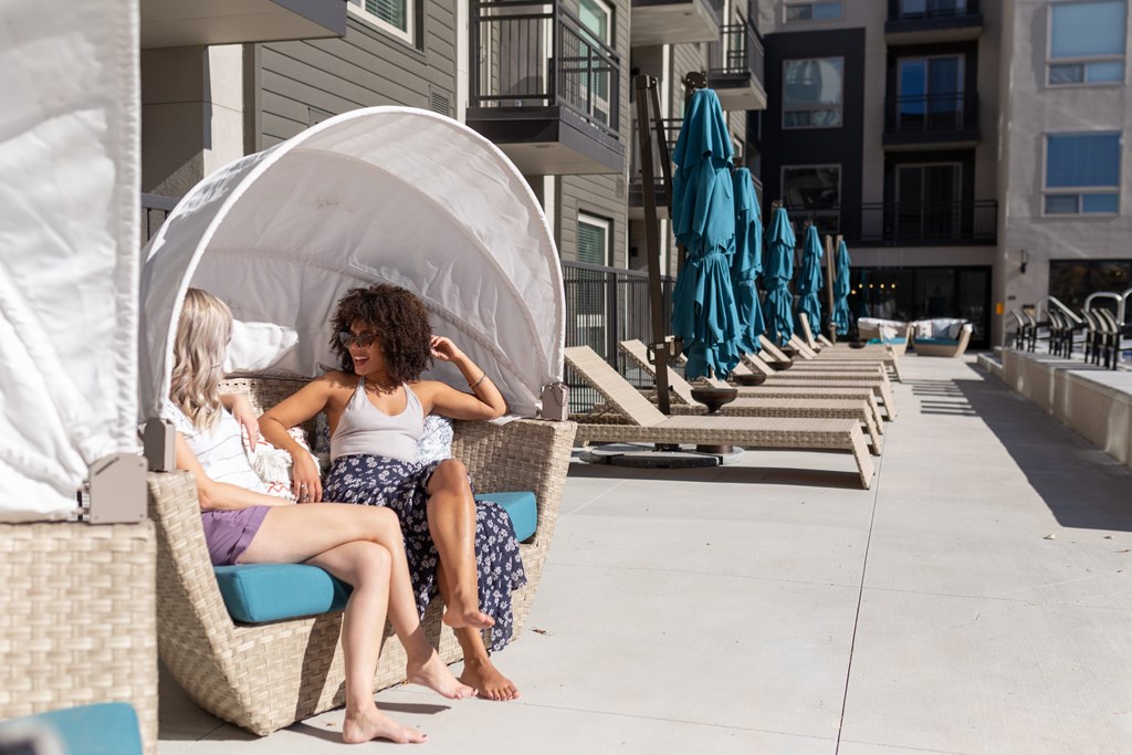 Two women are sitting on a blue cushioned chair on a patio.