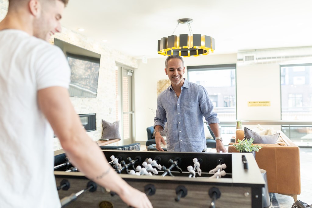 A man in a blue shirt is playing a game of foosball in a brightly lit room.