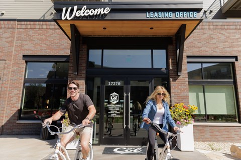 Two people riding bicycles in front of a leasing office.