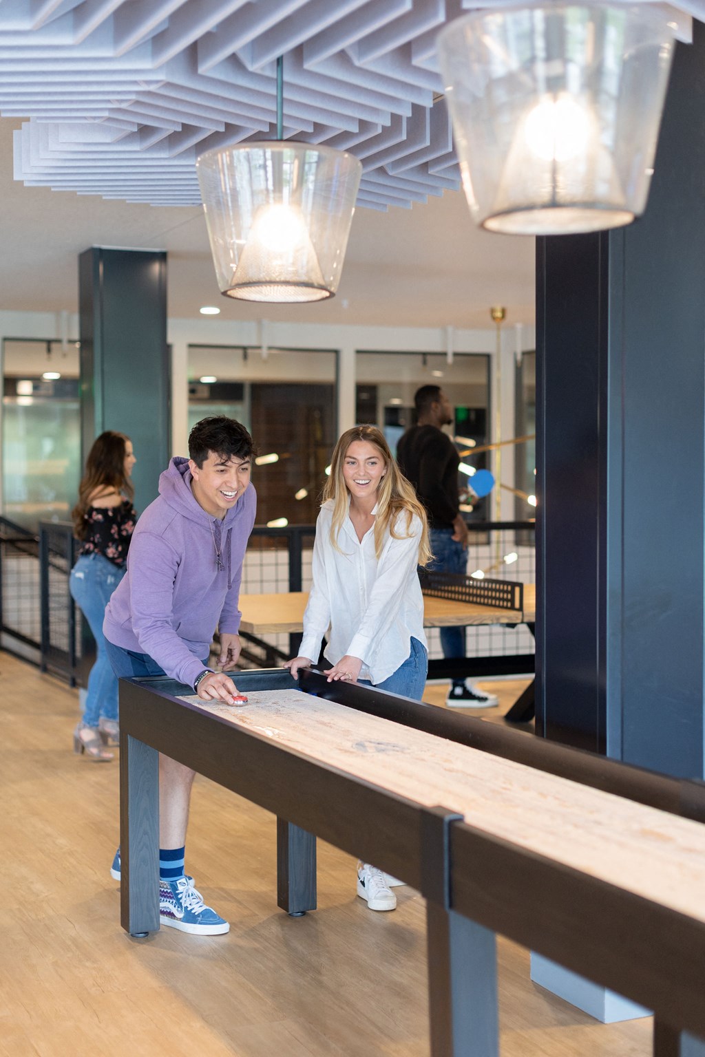 a man and a woman playing shuffleboard in a room with people in the background