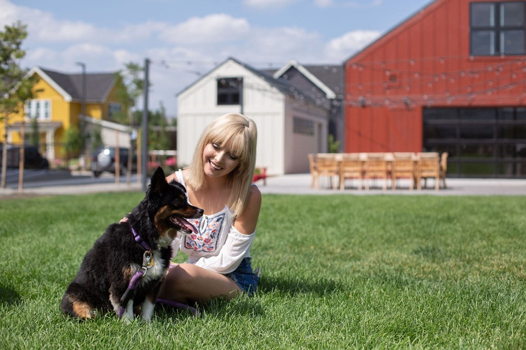 A woman is sitting on the grass with her dog.