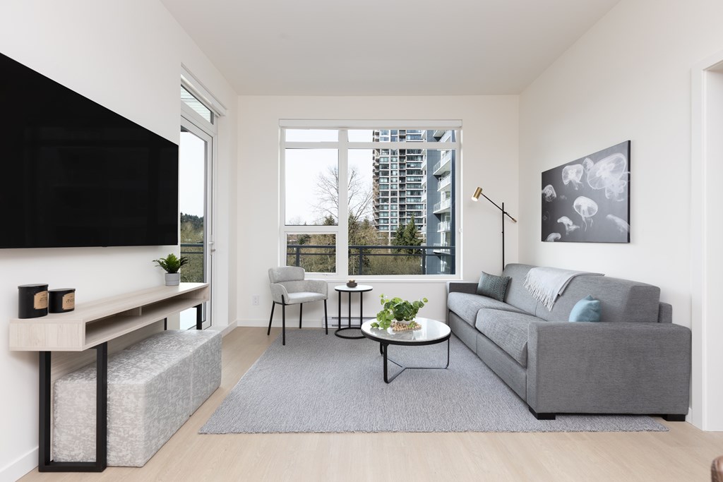 A living room with a grey couch, a black television, and a large window.