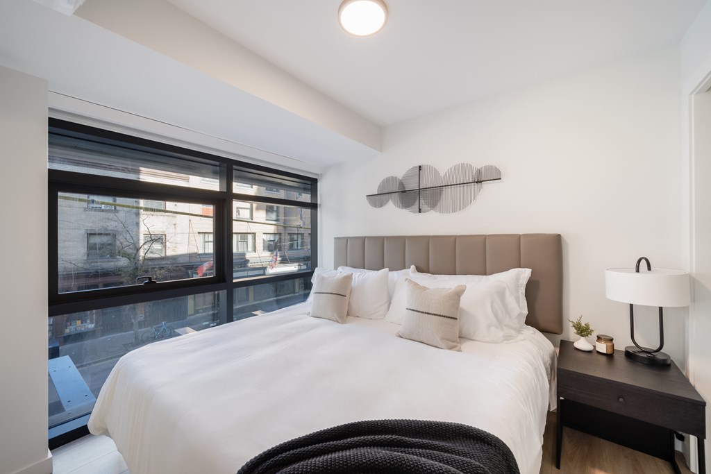 A bedroom with a large bed and a window overlooking a cityscape.