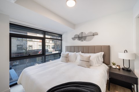A bedroom with a large bed and a window overlooking a cityscape.