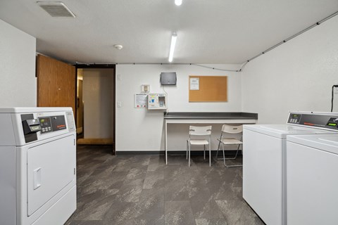 A clean, modern laundry room with a washer and dryer on the left and a counter with two chairs in the middle.