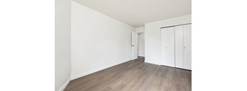 A room with white walls and wooden flooring with two white cupboards.