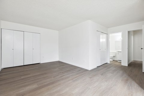 A room with white walls and wooden flooring with a white door on the right.