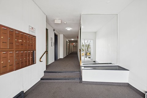 A long hallway with a row of brown lockers on the left and a staircase on the right.