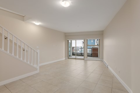 A spacious room with a staircase on the left and a doorway leading to another room on the right.