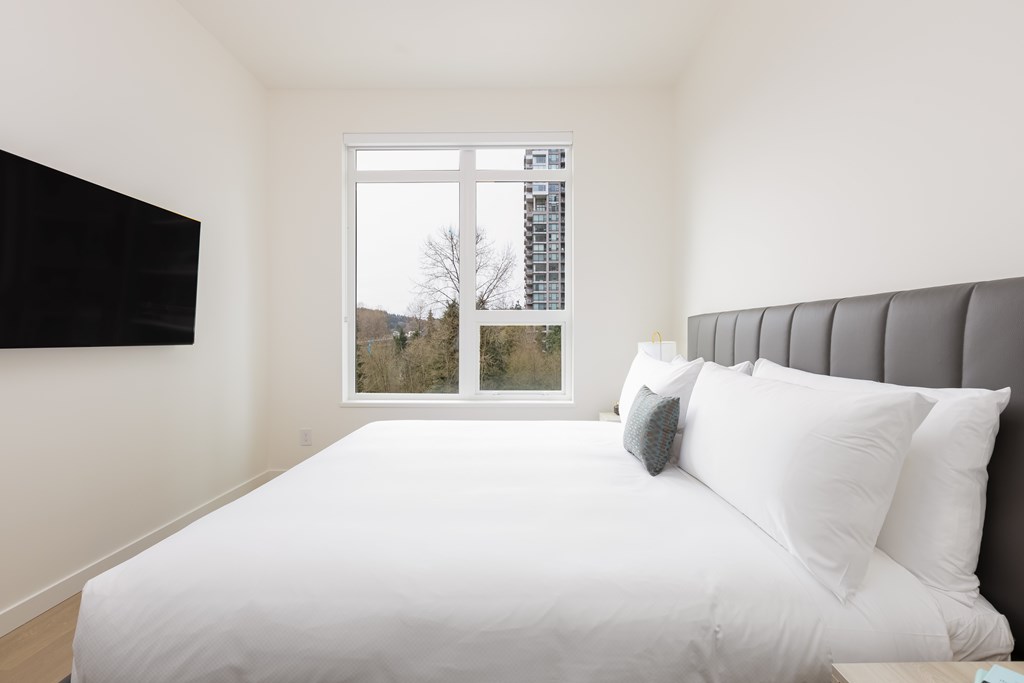 A white bed with a grey headboard and two pillows in a room with a window.