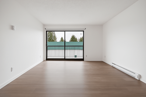 A room with a wooden floor and a large window with a view of trees.