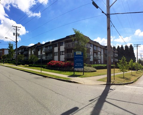 A street view of a residential area with apartment buildings and a sign for a real estate agency.