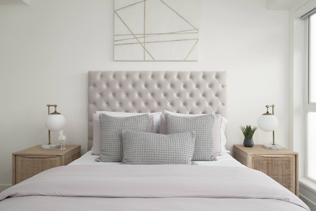 a white bedroom with a bed with pillows and a geometric painting on the wall