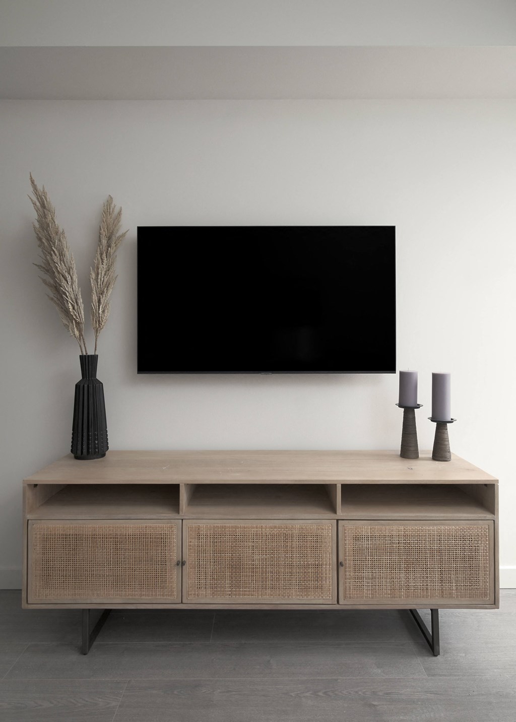 a television on the wall above a wooden shelf with a vase and two lamps