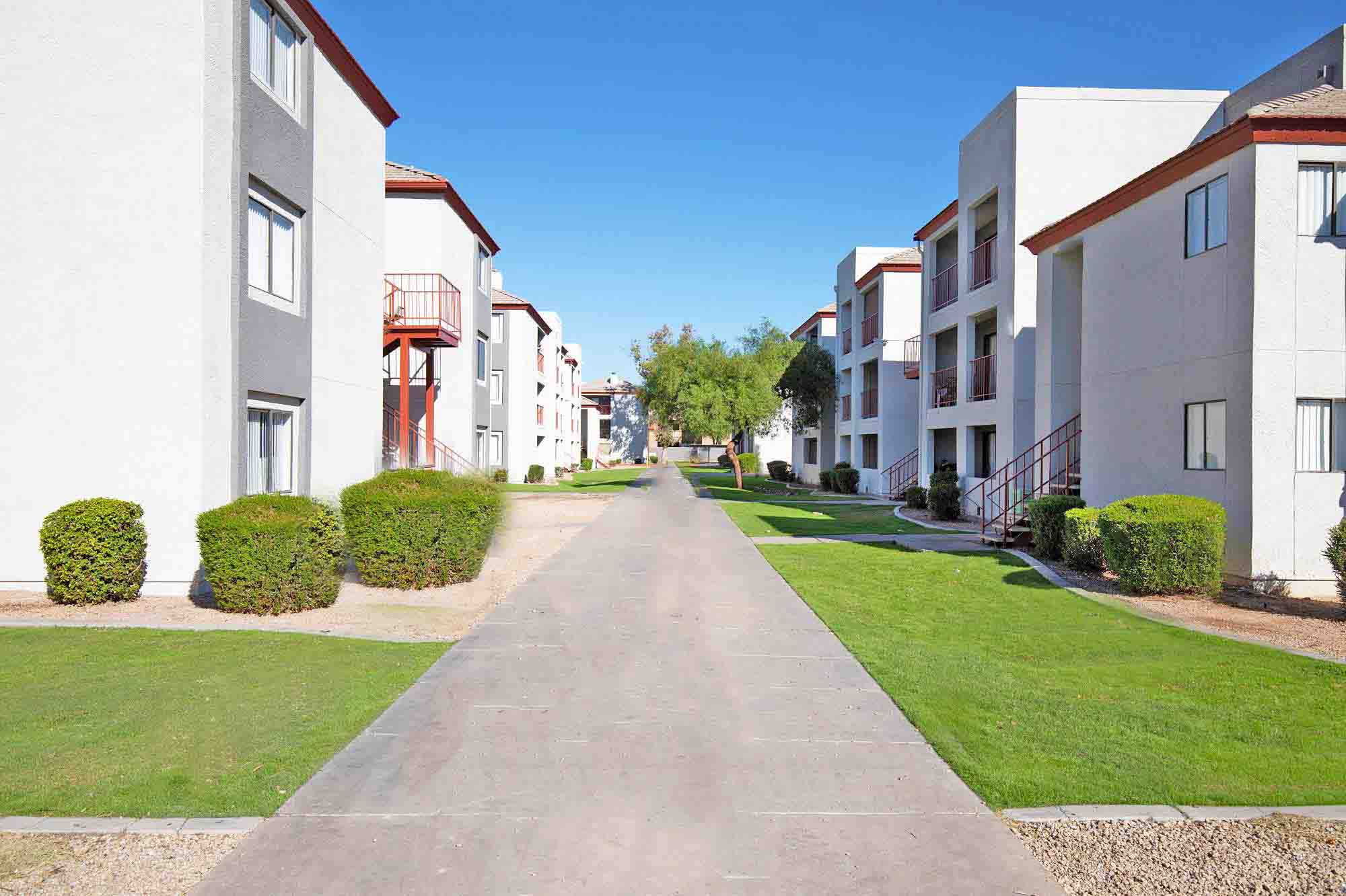 a pathway between modern apartment buildings with green grass
