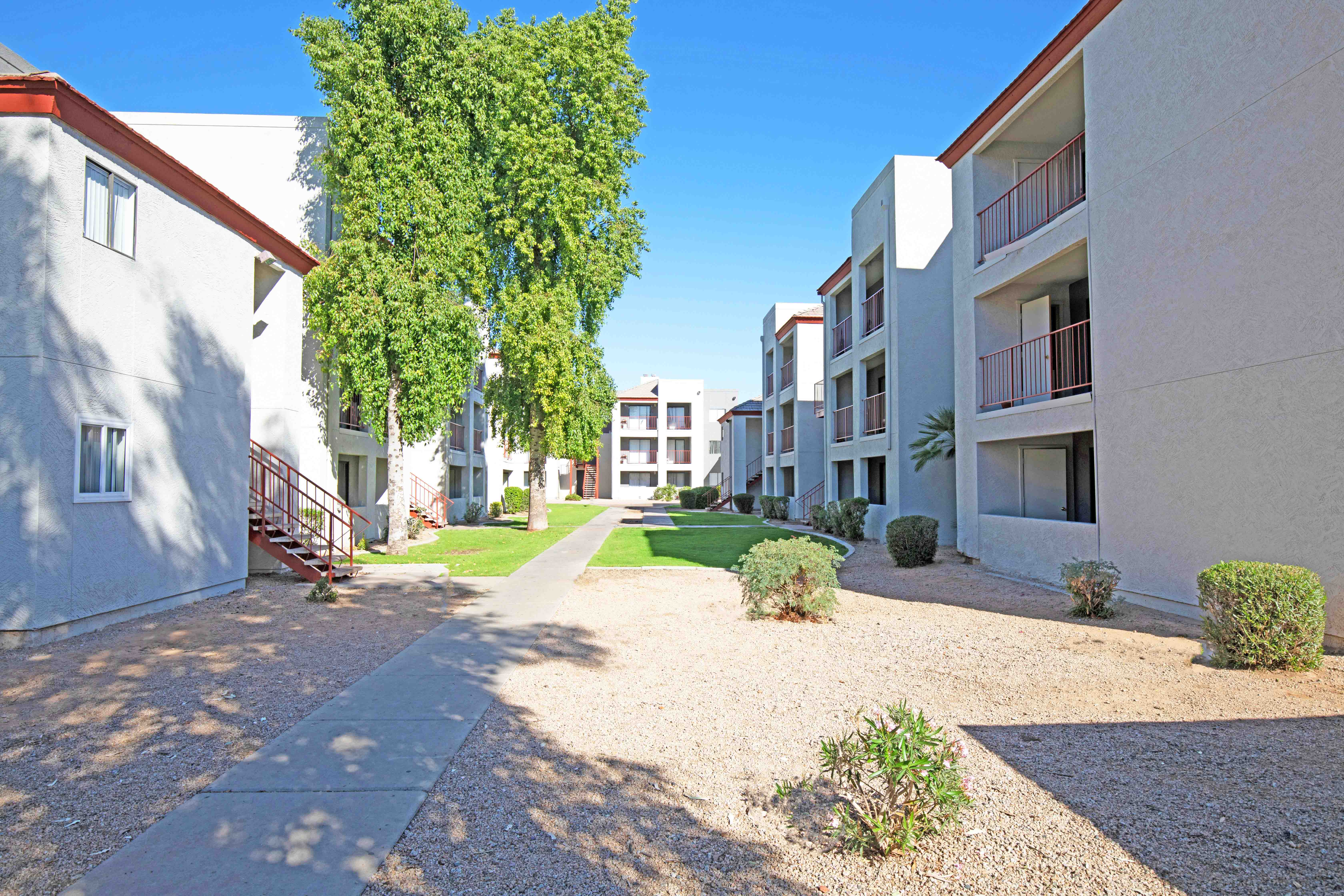 a pathway between two apartment buildings with green grass and trees