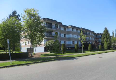 Apartment building with trees and bushes in front.