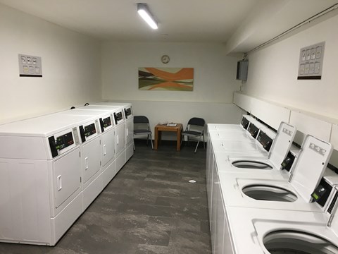 A laundromat with washers and dryers lined up on both sides of the room.